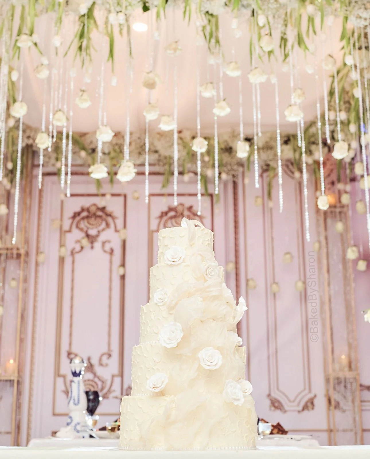 Five-tier white cake in a pink ballroom under hanging florals