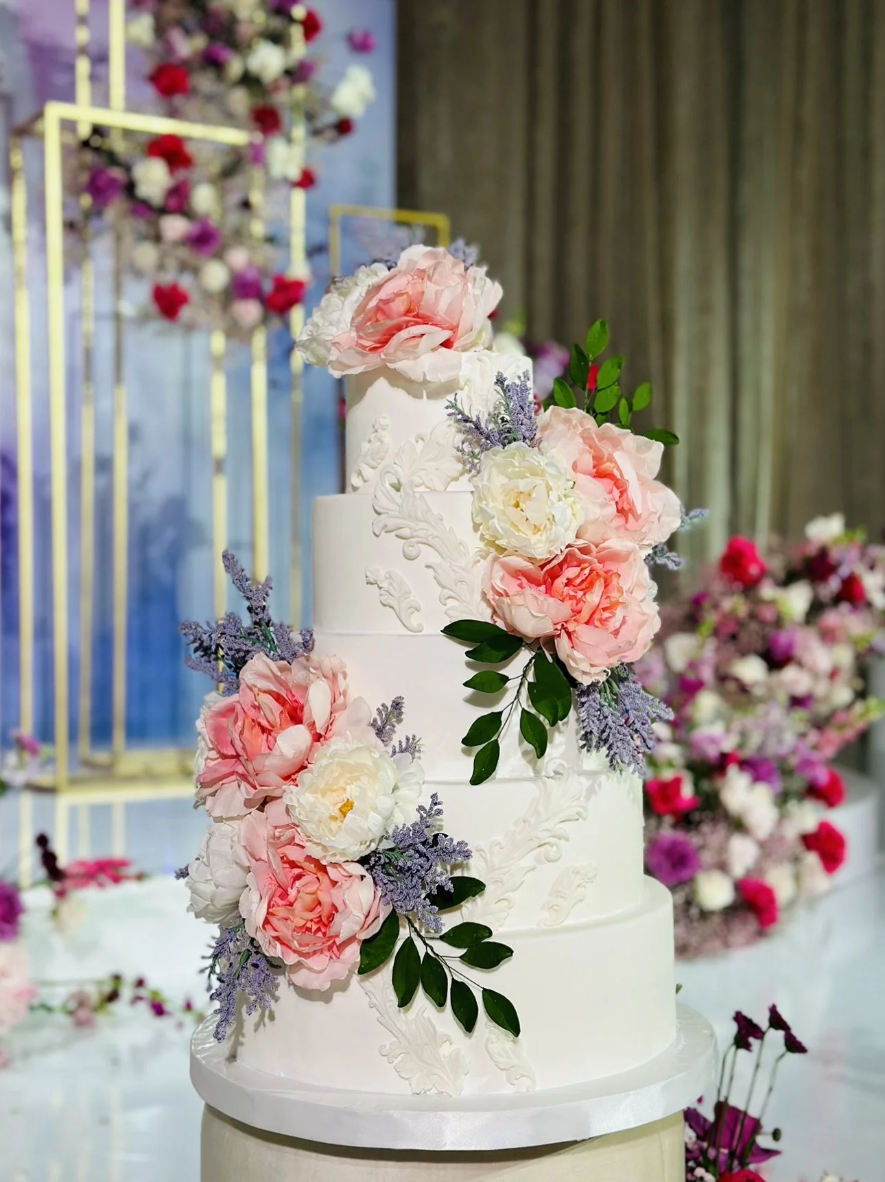 Tiered white wedding cake decorated with pink roses and lavender