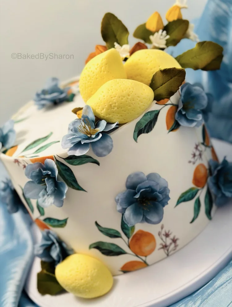 White cake painted with blue flowers and topped with lemons