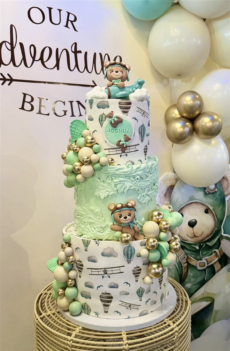 Adventure-themed baby shower cake with a teddy bear topper and balloons
